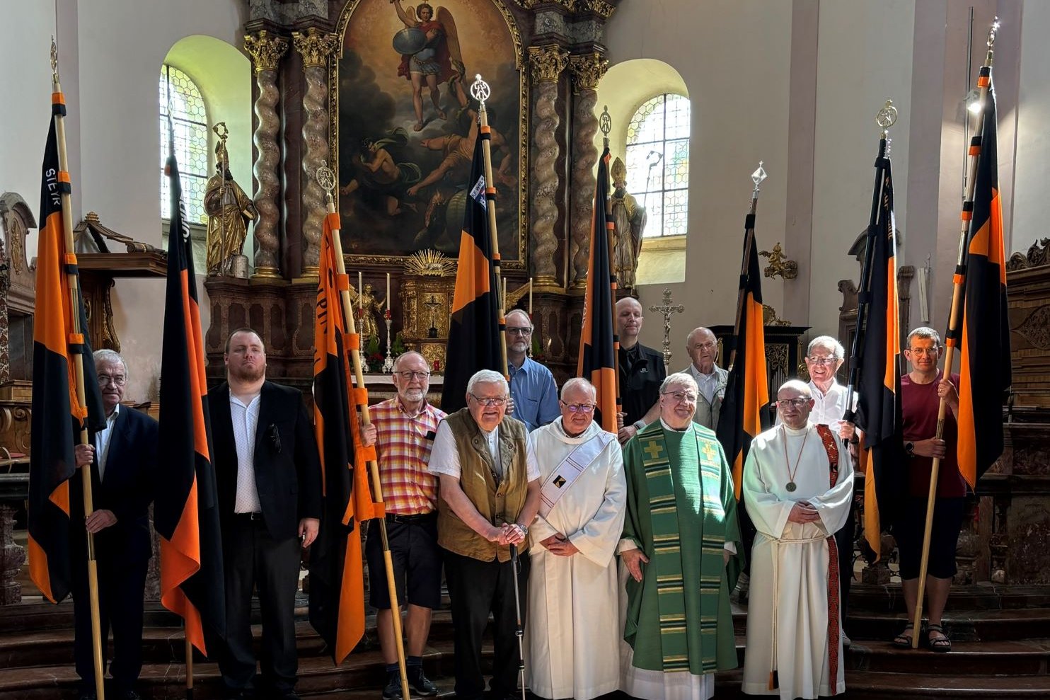 Vereinsmitglieder und Priester mit Fahnen vor dem Altar des Stifts