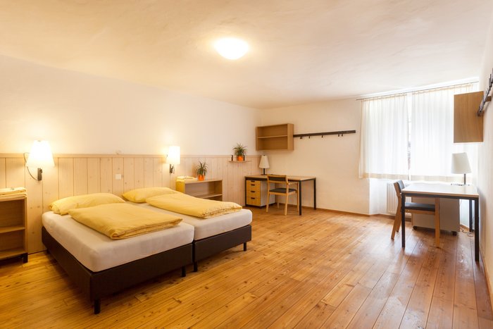 Möbliertes Zimmer im Kolpinghaus Hallein mit Bett, Schreibtisch und Stauraum.